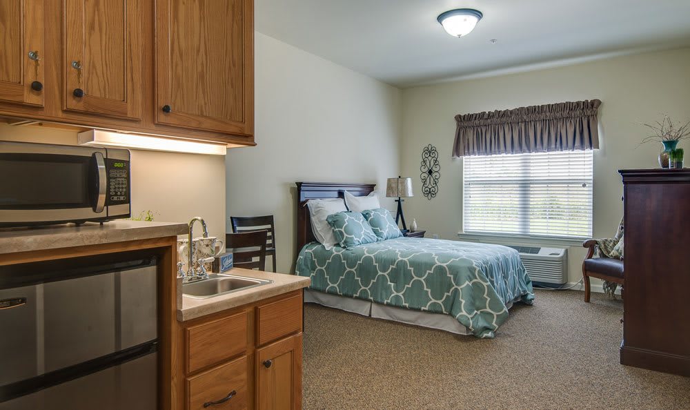 A cozy bedroom with a neatly made bed, wooden cabinets, and a window letting in natural light.