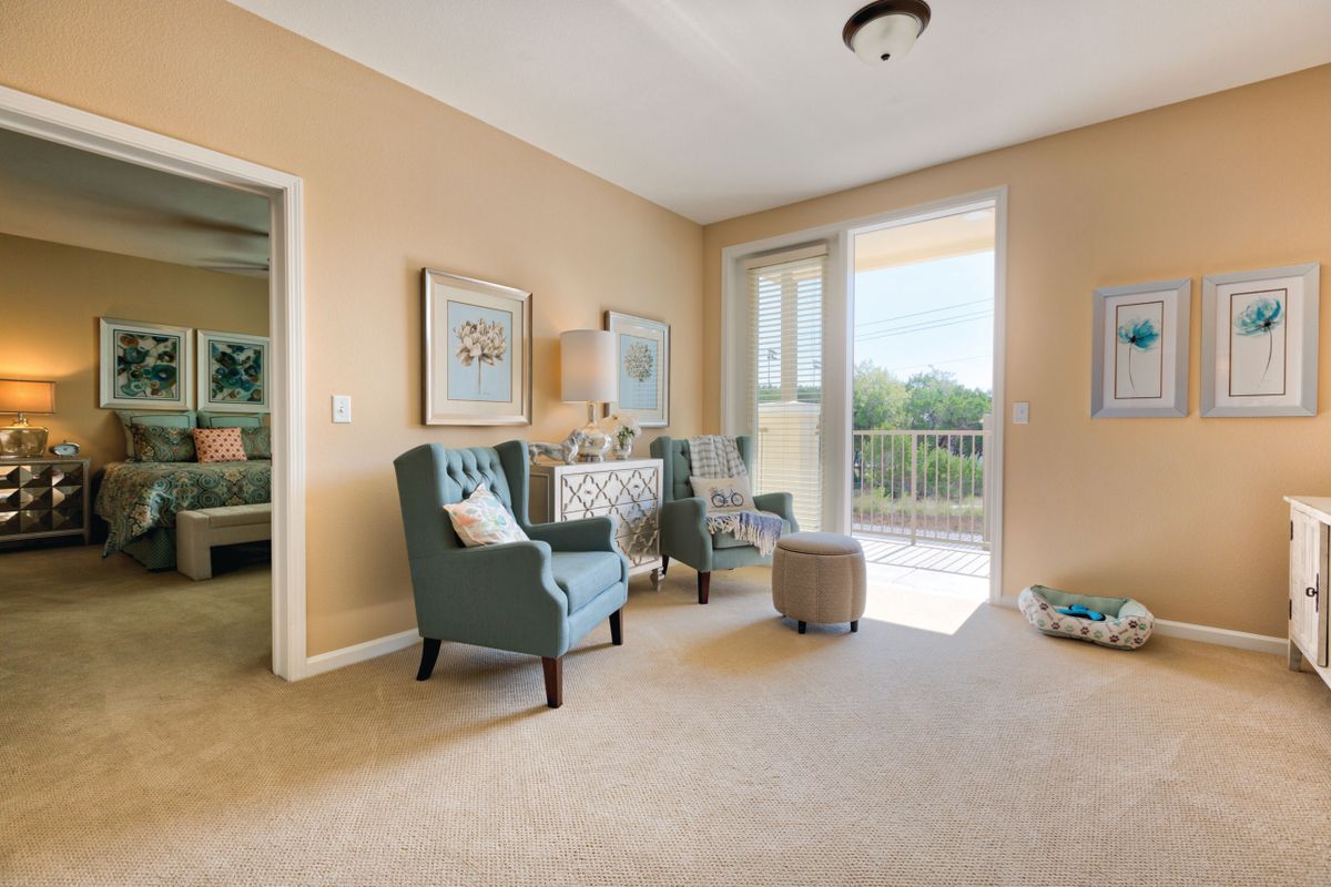 A bright living room with comfortable chairs, a small side table, and access to a balcony.