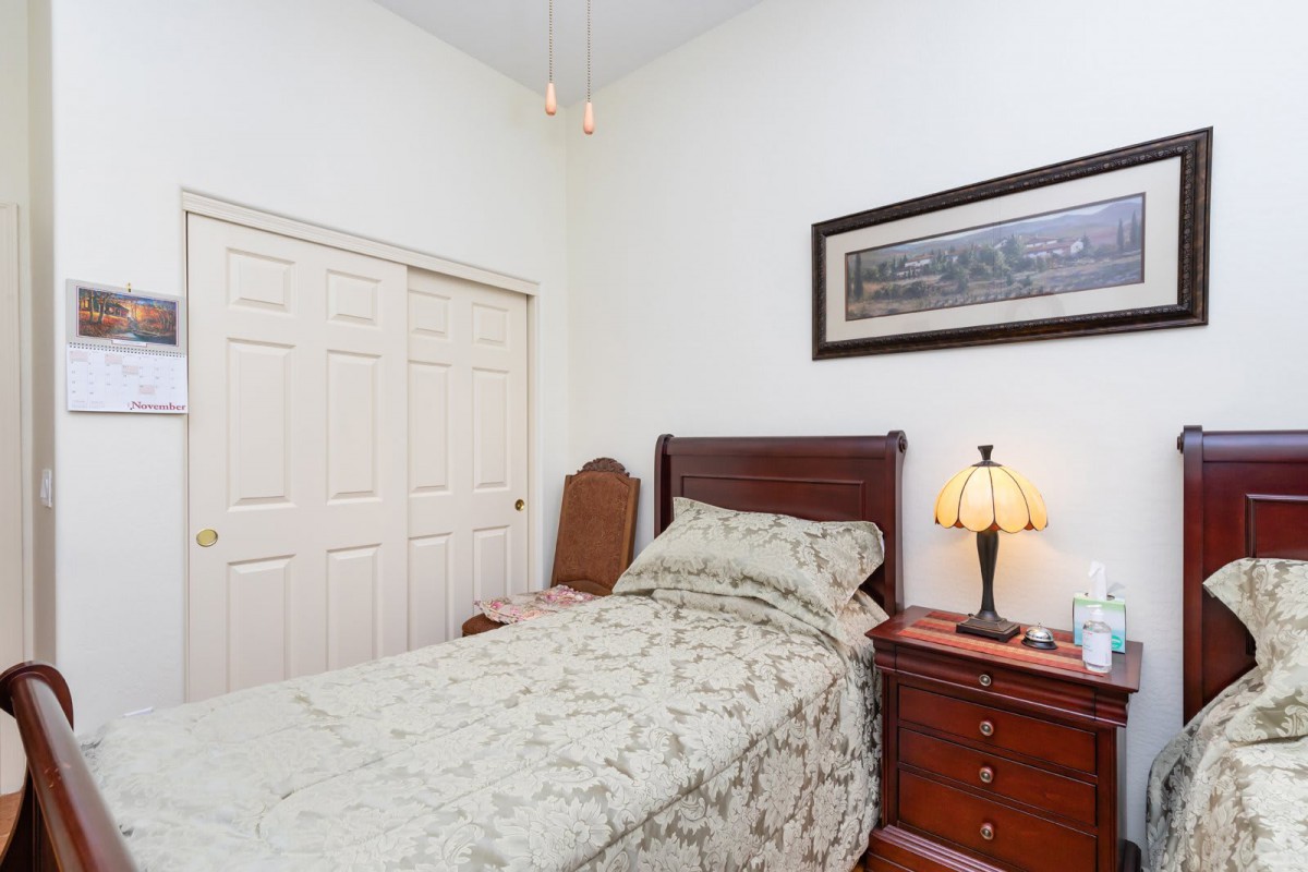 A neatly arranged bedroom with a single bed and wooden furniture, featuring a cozy lamp and artwork on the wall.