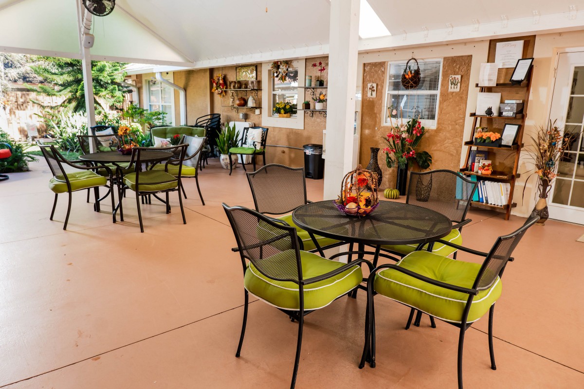 A beautifully decorated patio with tables and green-cushioned chairs, surrounded by plants.