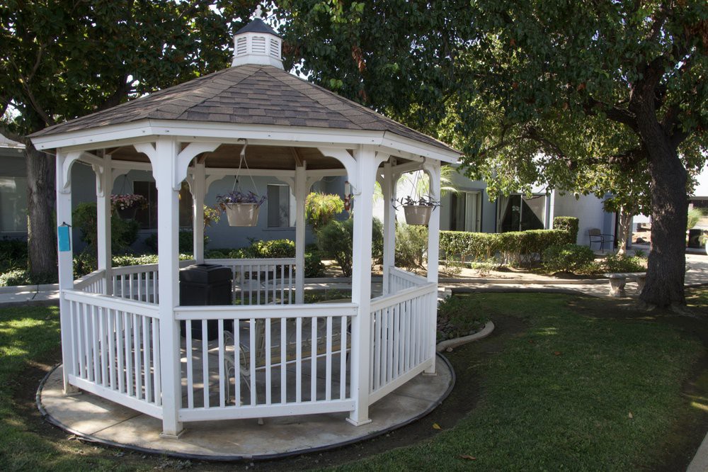 A white gazebo surrounded by a well-maintained garden with lush green grass and trees.