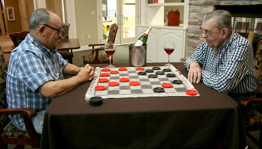 Two friends enjoying a game of checkers with glasses of wine and champagne on the table.
