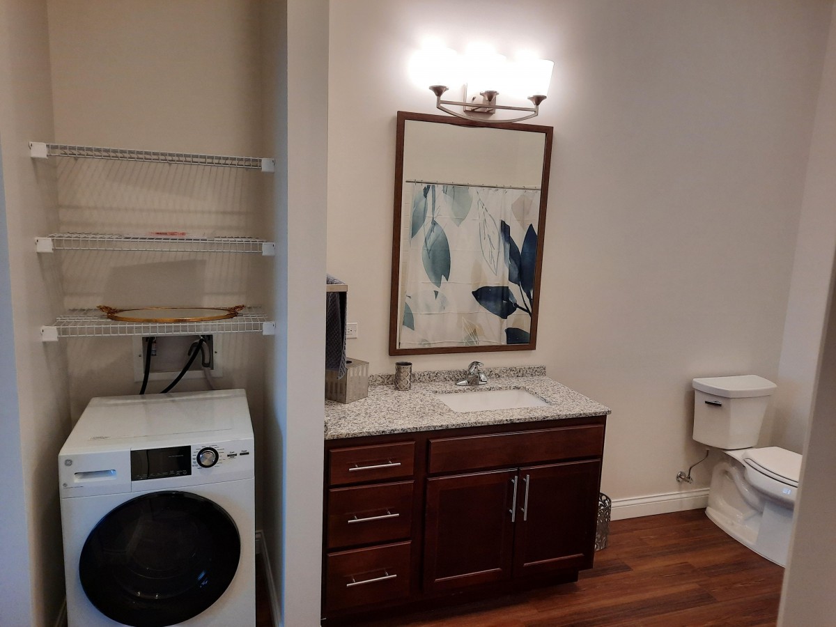 A combined bathroom and laundry area featuring a vanity with a mirror, a washer/dryer unit, and wall artwork.