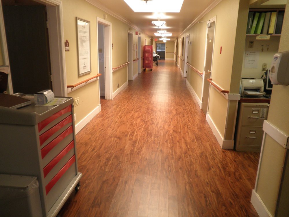 A hospital corridor with a medical cart and open doors along the hallway.