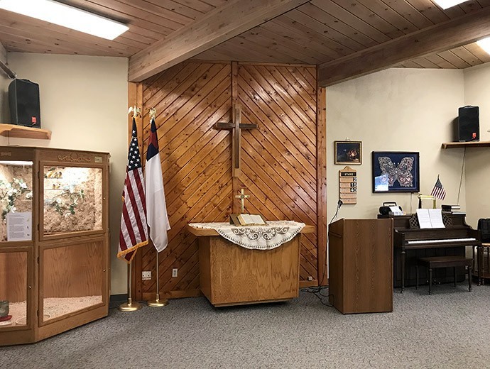 A church interior featuring a wooden altar with a cross, flanked by American and Christian flags, alongside a pulpit.
