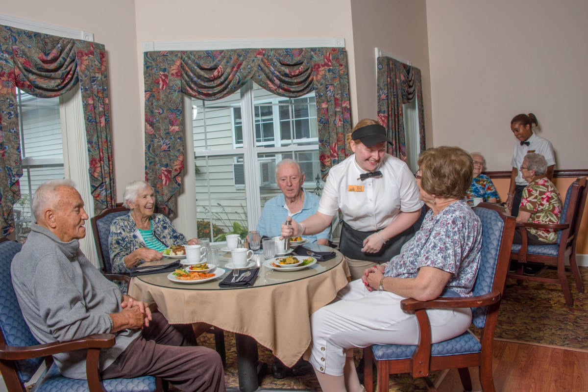 A group of seniors enjoying a meal together at a restaurant, served by a waiter.