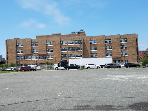 A brick building with multiple windows and parked vehicles in the foreground.