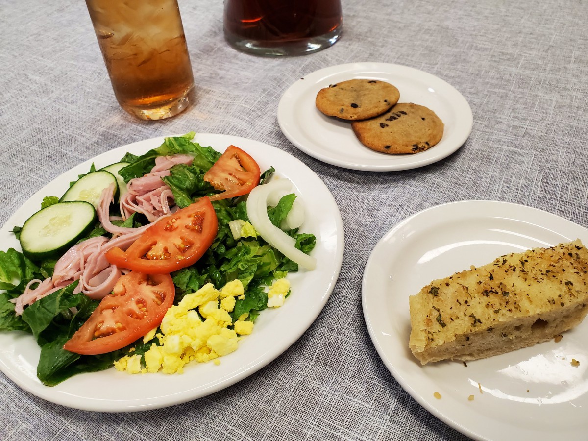 A meal featuring a fresh salad with tomatoes, onions, and cucumbers, accompanied by cornbread, cookies, and a glass of iced tea.