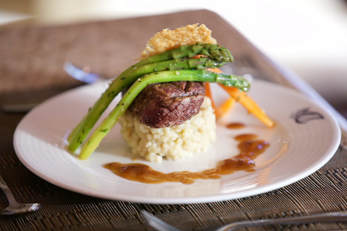 A gourmet steak dish beautifully plated with asparagus and rice, garnished with a sauce.