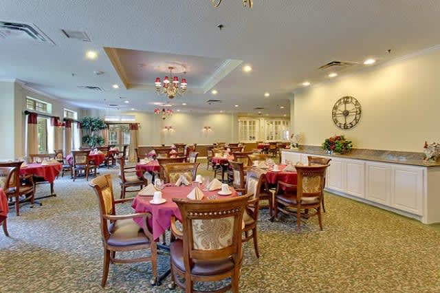 A spacious and elegantly decorated dining room with round tables set for meals, featuring chandeliers and a cozy ambiance.
