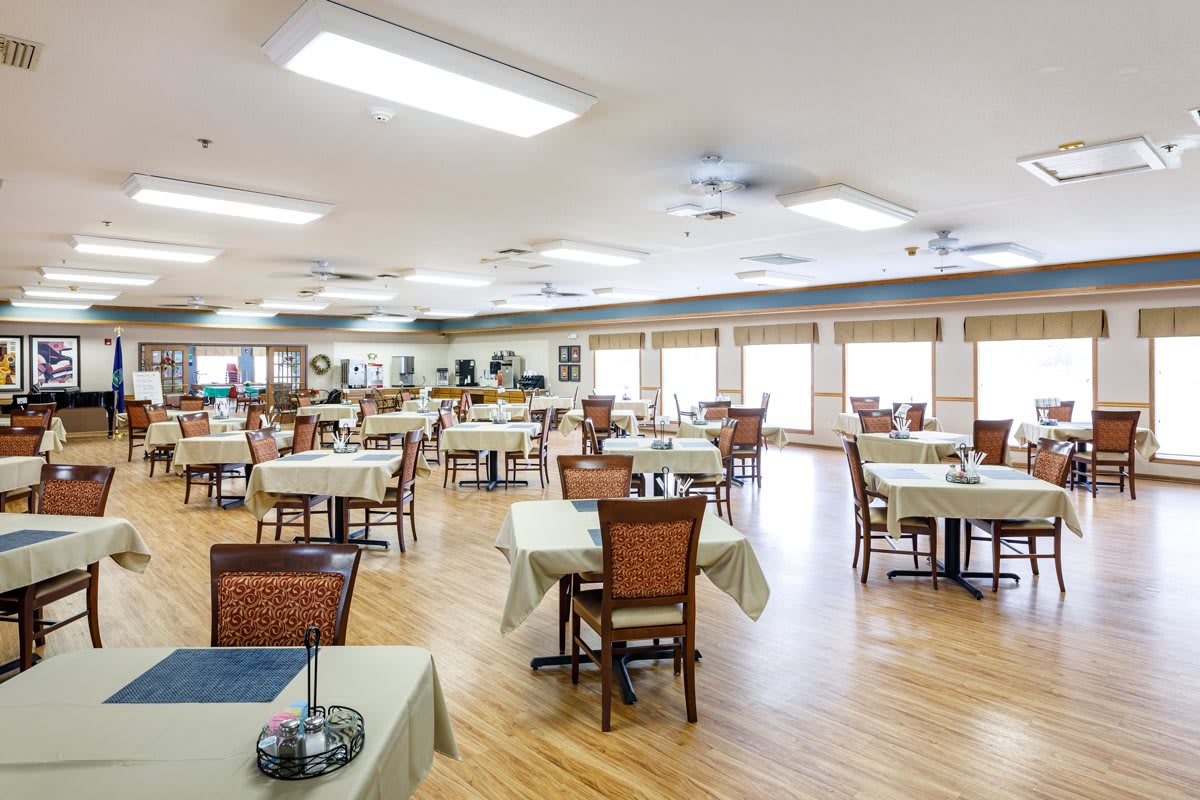 A spacious dining area with neatly arranged tables and chairs, featuring bright lighting and a wooden floor.