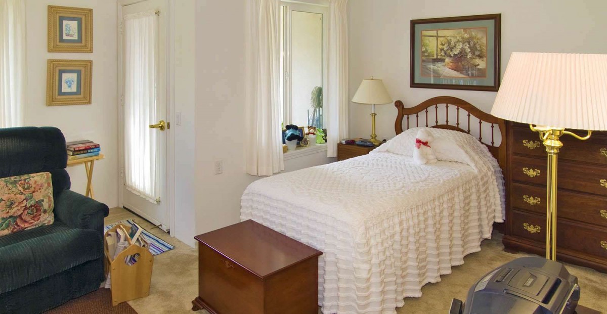 A cozy bedroom with a single bed, bedside lamp, and a mirror on the wall.