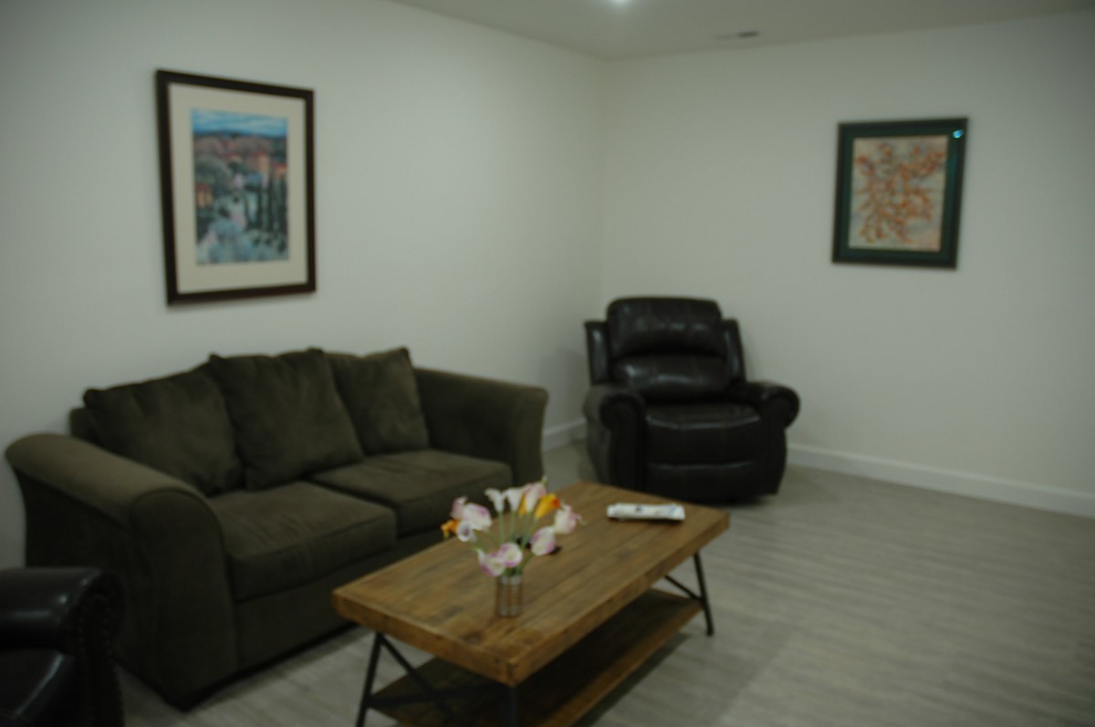 A cozy living room featuring a sofa, reclining chair, coffee table with flowers, and wall artwork.
