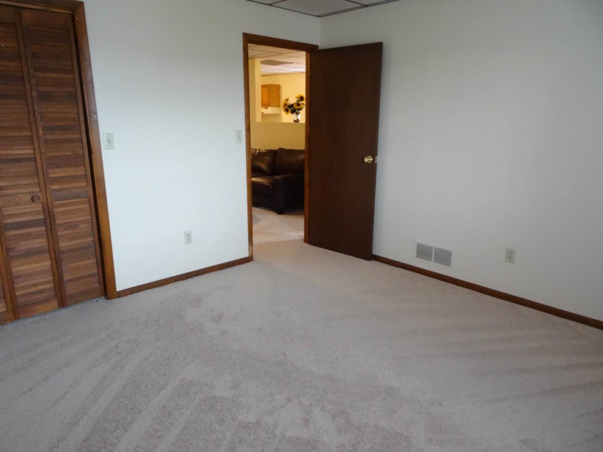 A carpeted empty room with an open door leading to another space.