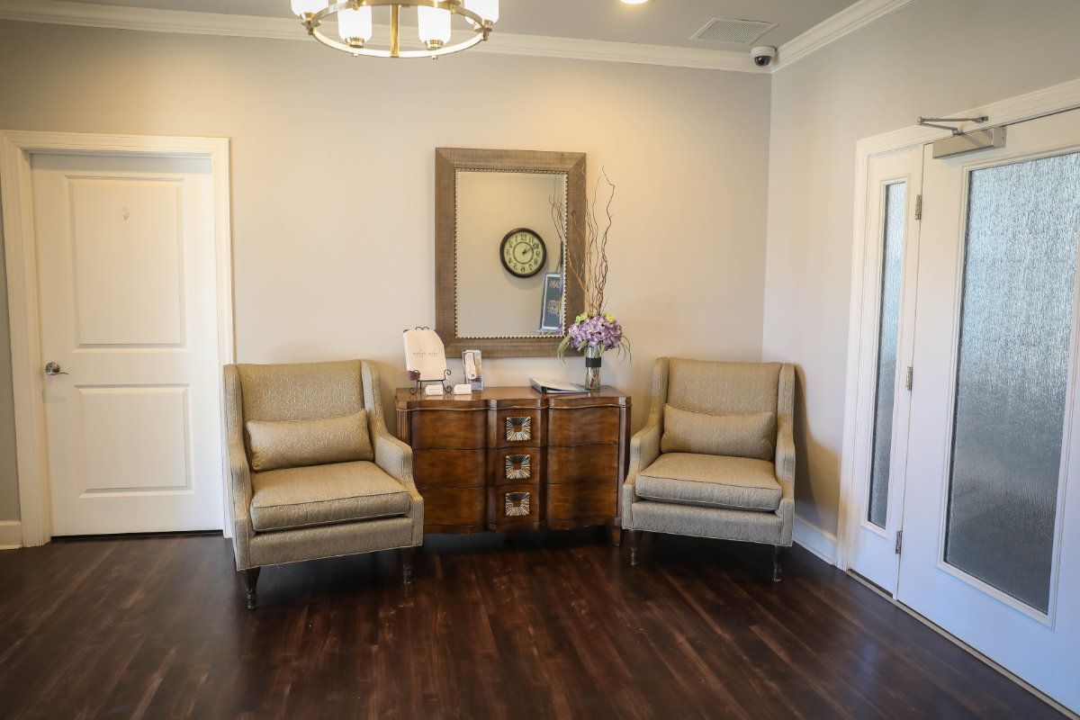A cozy waiting room with two armchairs, a wooden cabinet, and a mirror on the wall.
