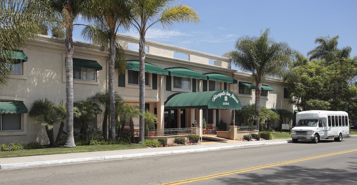 A hotel building with green awnings, situated alongside a street lined with palm trees.