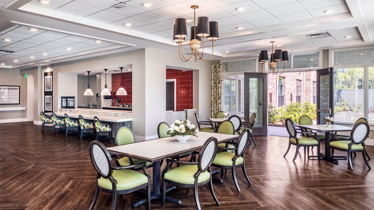 A modern dining area with elegant chandeliers, green upholstered chairs, and a sleek table on wooden flooring.