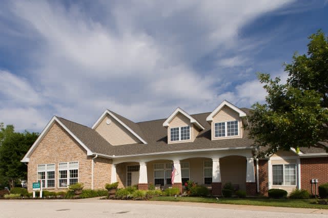 A suburban residential house with a brick exterior under a partly cloudy sky.