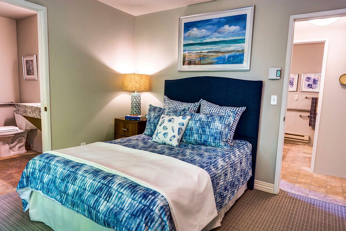 A cozy bedroom with a blue-themed bedding set, a bedside lamp, and artwork above the bed.