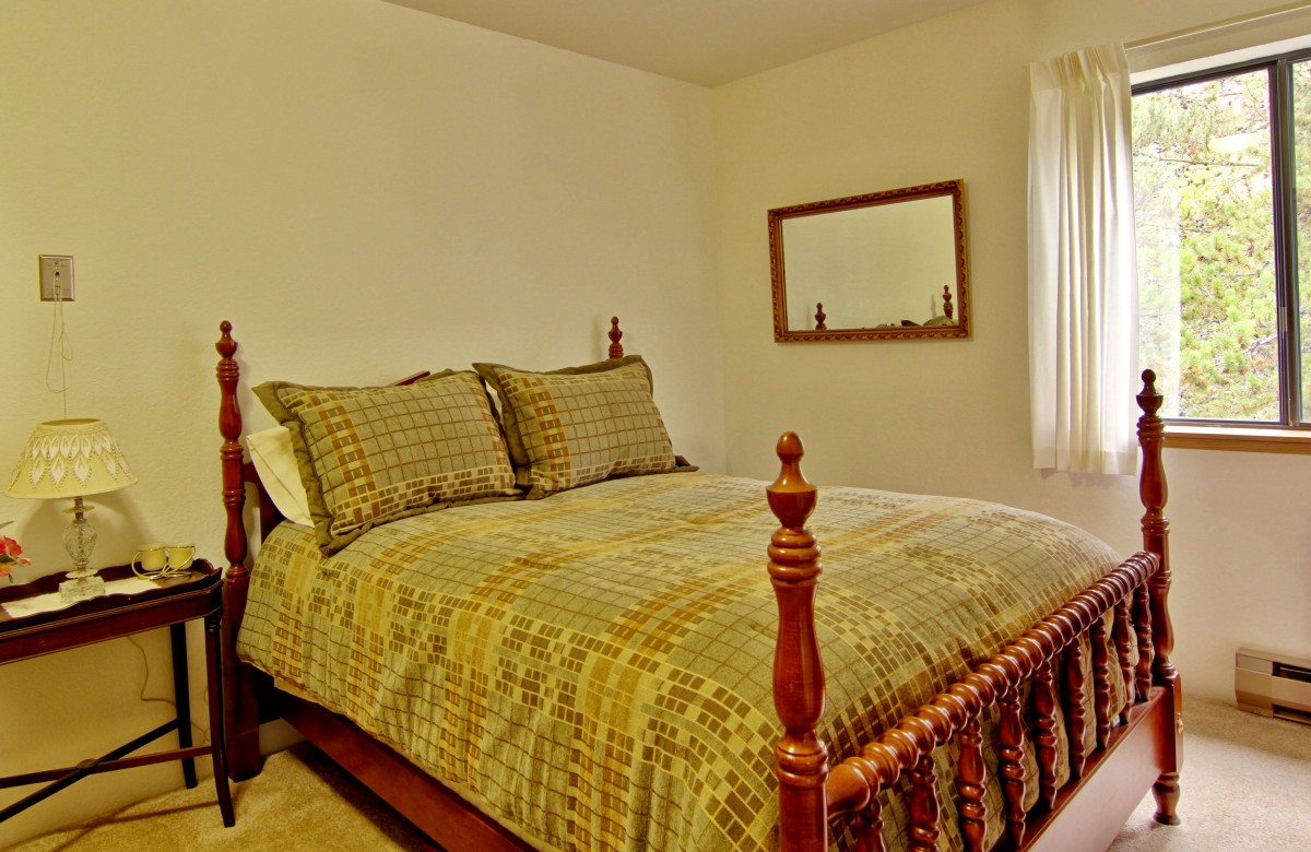 A cozy bedroom with a traditional wooden bed and patterned bedding, featuring a mirror on the wall.