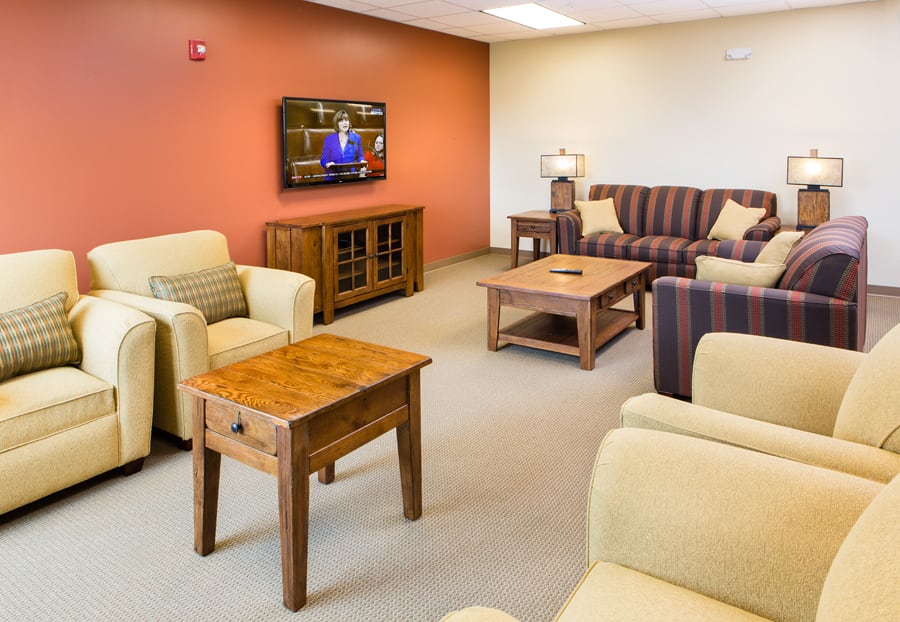 A cozy living room with comfortable sofas, chairs, and a television on the wall.