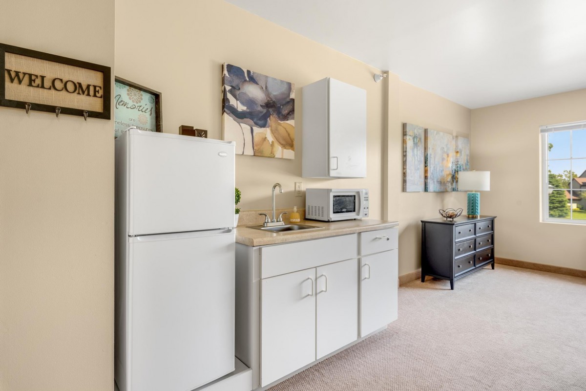 An apartment kitchen with a fridge, microwave, and cabinets, decorated with artwork on the walls.
