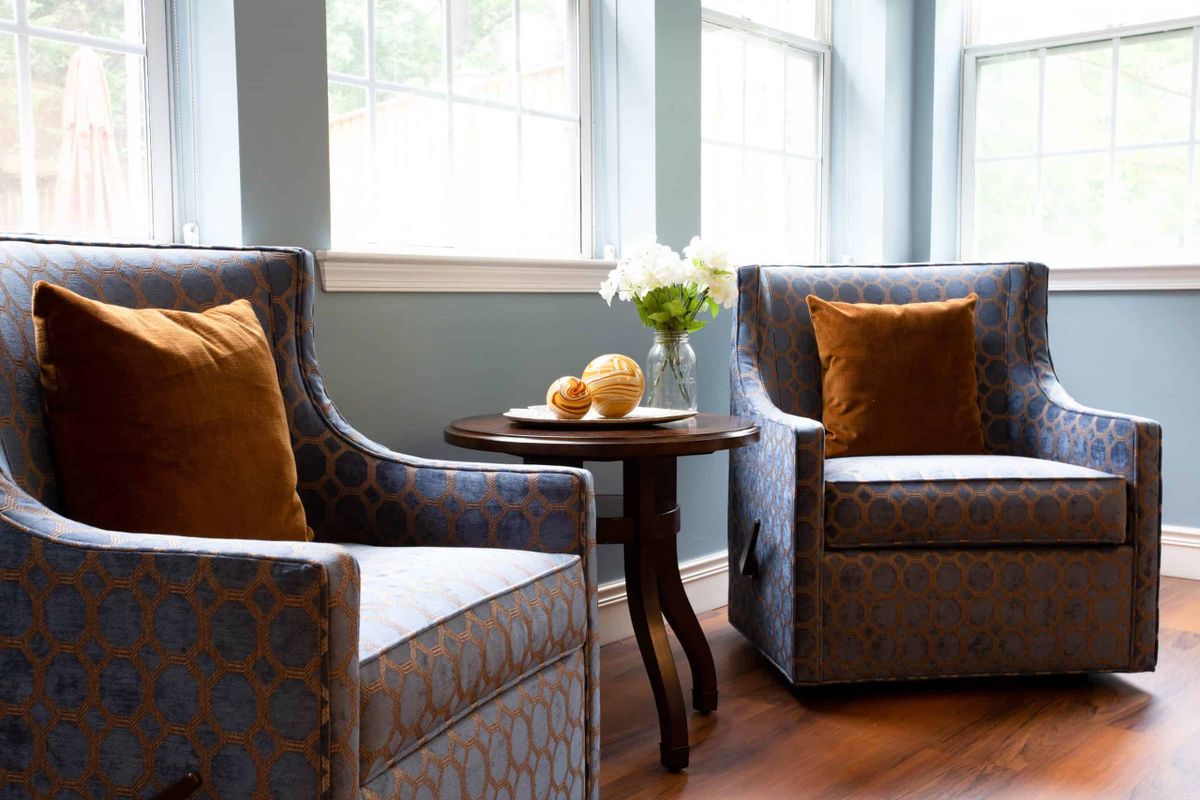 A cozy living room corner with two armchairs, a small round table, and a bright window.
