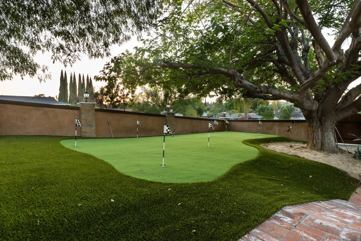 A serene backyard putting green surrounded by trees.