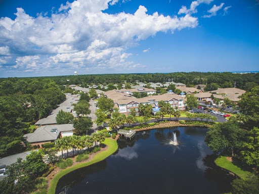 A serene aerial view of a residential community featuring a picturesque lake and lush greenery under a partly cloudy sky.