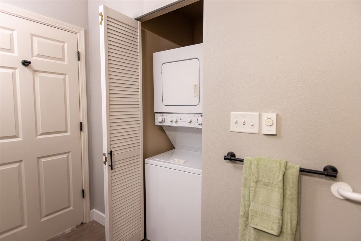 A stacked washer and dryer set inside a small closet with a partially open door.