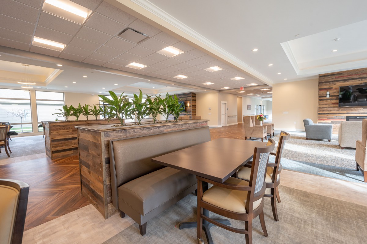 A modern dining area with wooden tables and chairs, accented by greenery and ambient lighting.