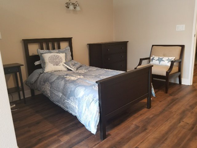 A simple bedroom with a bed, chair, and dresser on a wooden floor.