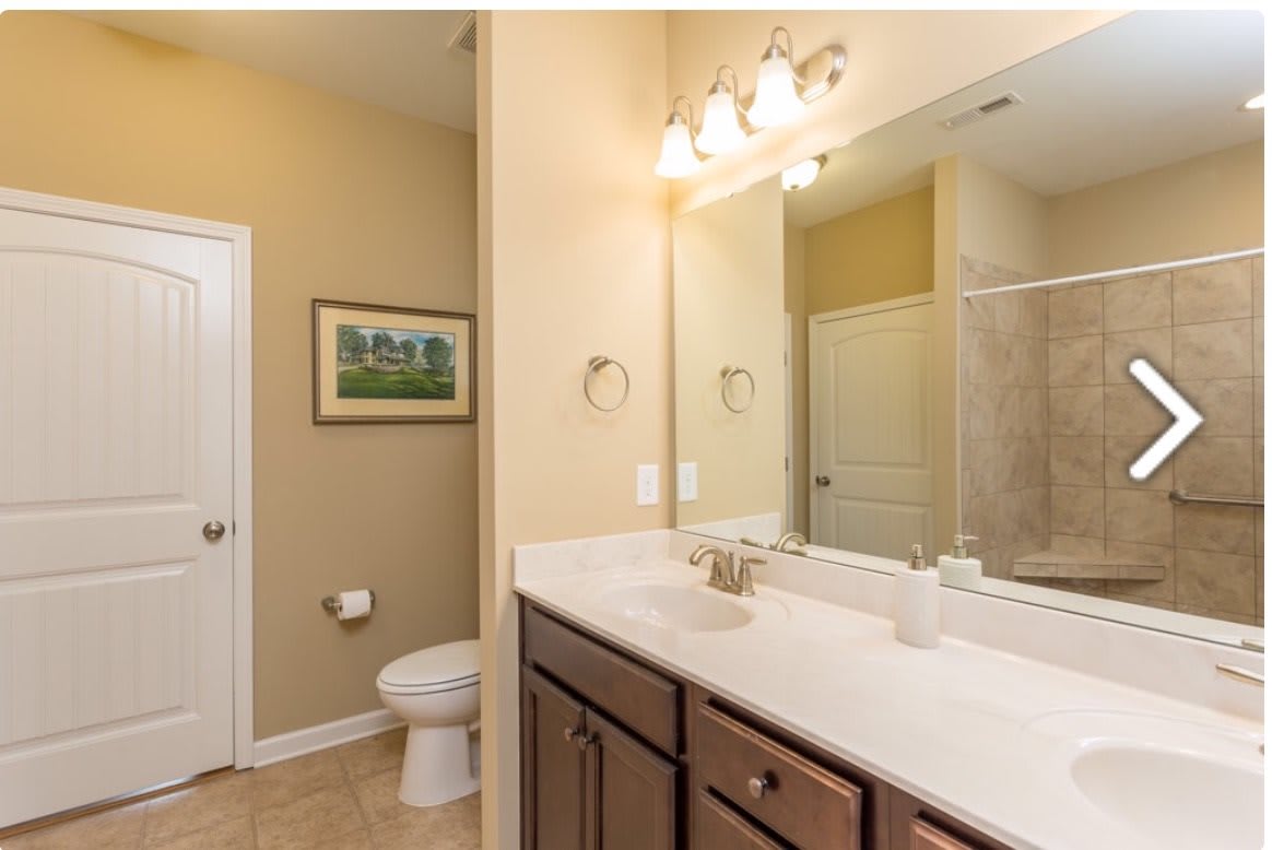 A clean and well-lit bathroom featuring a large mirror, sink with vanity, toilet, and shower.