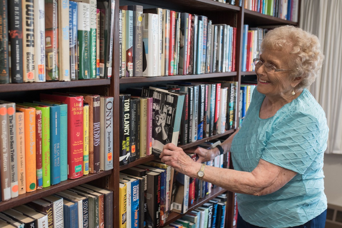 An elderly woman browsing books on a library shelf.