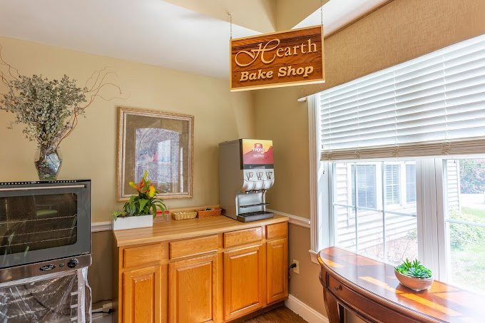A cozy bake shop interior featuring a wooden cabinet, beverage dispenser, and a sign hanging above.
