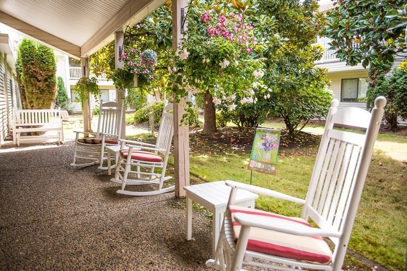 A cozy porch with white rocking chairs overlooking a lush garden filled with flowers and greenery.