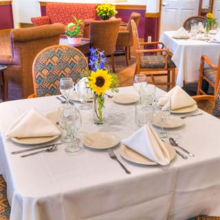 A neatly set dining table with white napkins, glassware, and a floral centerpiece in a restaurant setting.
