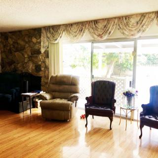 A cozy living room featuring a mix of recliners and chairs, with large windows covered by drapes, and a decorative stone wall.