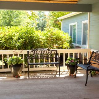 A cozy porch with metal benches and potted plants, surrounded by lush greenery.