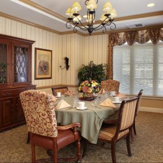 An elegantly decorated dining room featuring a chandelier, a set table with chairs, and a cabinet against striped wallpaper.