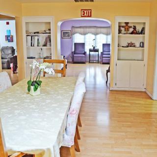 A cozy dining room with a wooden table, chairs, and an orchid centerpiece, leading to an adjoining sitting area.