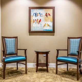A cozy waiting area with two chairs, a small table, and a colorful painting on the wall.