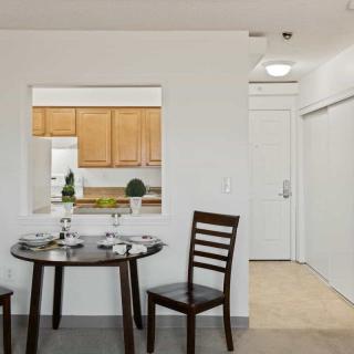 A modern dining area with a small table and two chairs, offering a view into the kitchen.