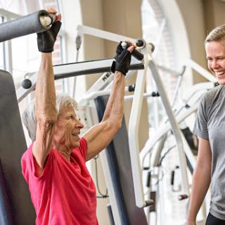An older adult engages in strength training with the assistance of a personal trainer at the gym.