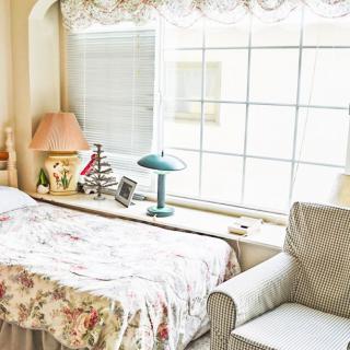 A cozy bedroom with a bed, lamp, and armchair next to a large window.
