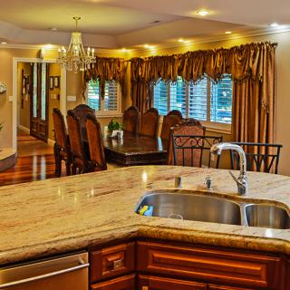 A luxurious kitchen and dining area featuring granite countertops, elegant wood cabinets, and a chandelier.