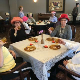 Elderly women enjoying a tea party while wearing colorful hats.