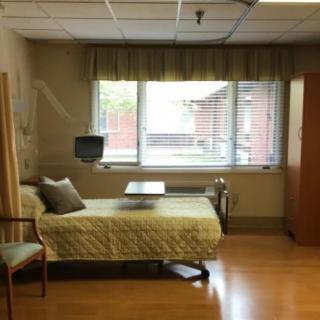 A hospital room with a bed, chair, television, and large window.