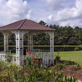 A charming gazebo surrounded by lush greenery under a partly cloudy sky.