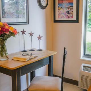 A cozy workspace featuring a small desk adorned with a vase of flowers and decorative art on the walls.